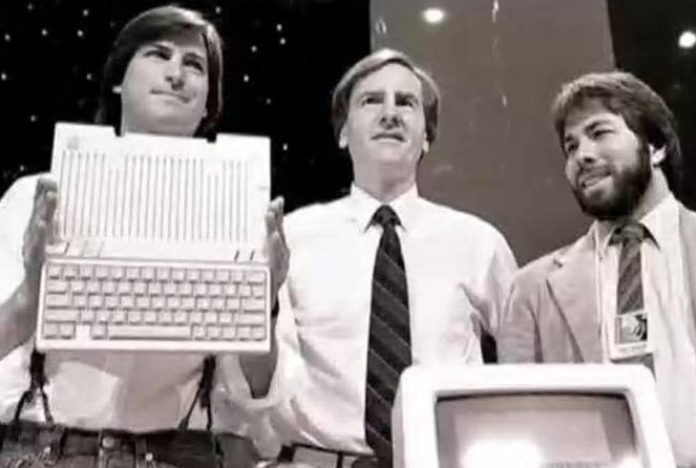 Fotografía de (de izquierda a derecha): Steve Jobs, Ronald Wayne y Steve Wozniak, Jobs sostiene la caja del Apple I en una feria de tecnología.